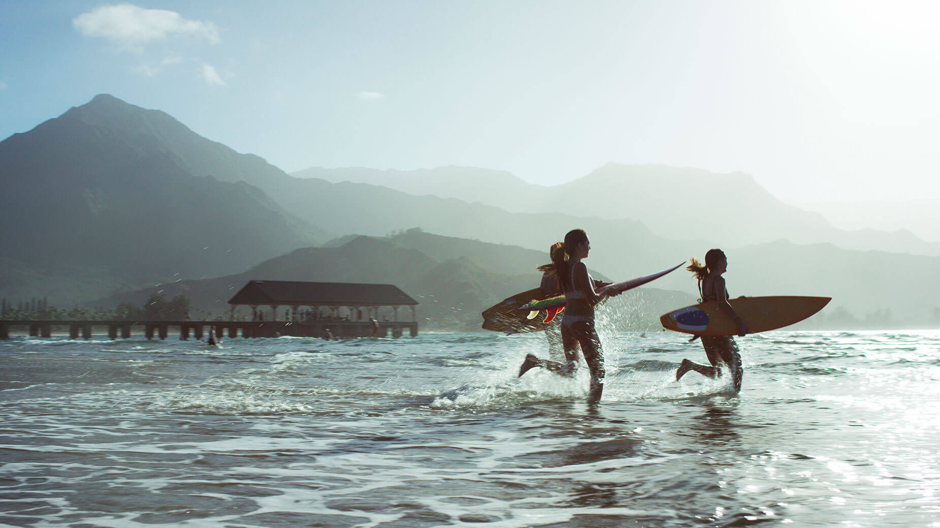 surfers running into the water carrying surf boards